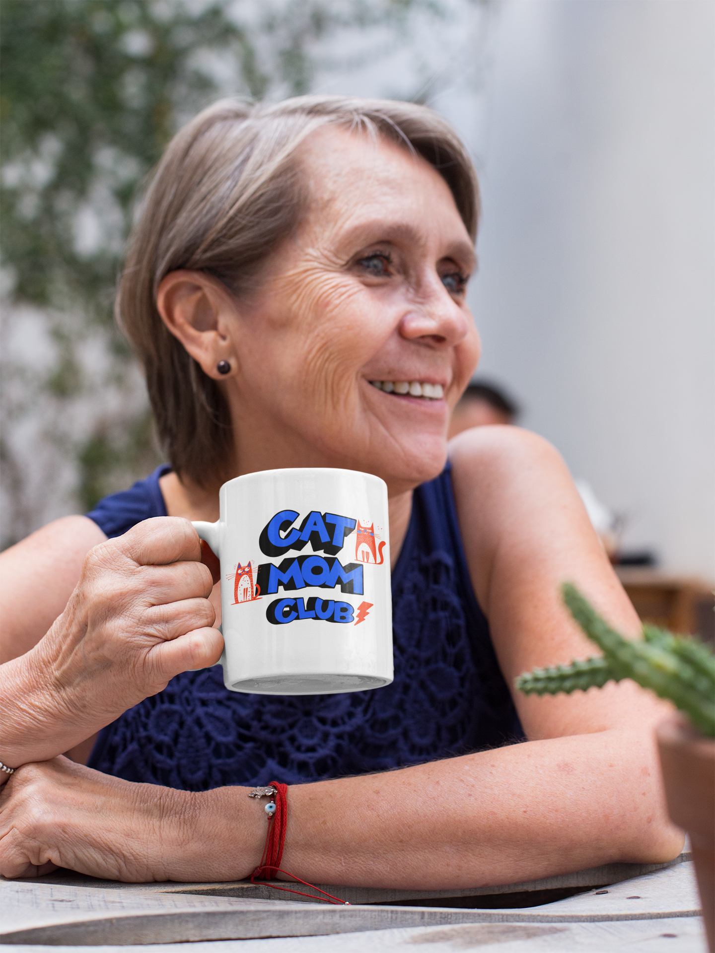 Smiling elderly woman holding Cat Mom Club 11oz mug at a table — perfect gift for cat moms of all ages
