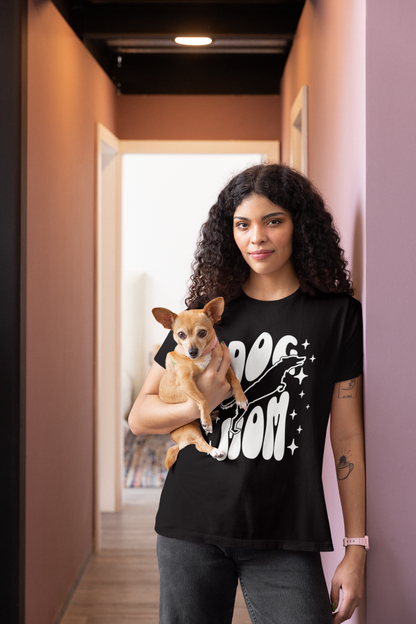 Woman holding a small dog wearing a black t-shirt with 'DOG MOM' text in a hallway.