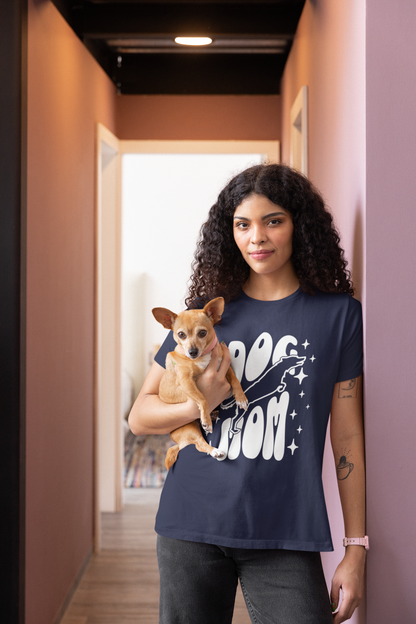 Woman wearing a navy blue t-shirt with 'Dog Mom' text, holding a small dog in a hallway.