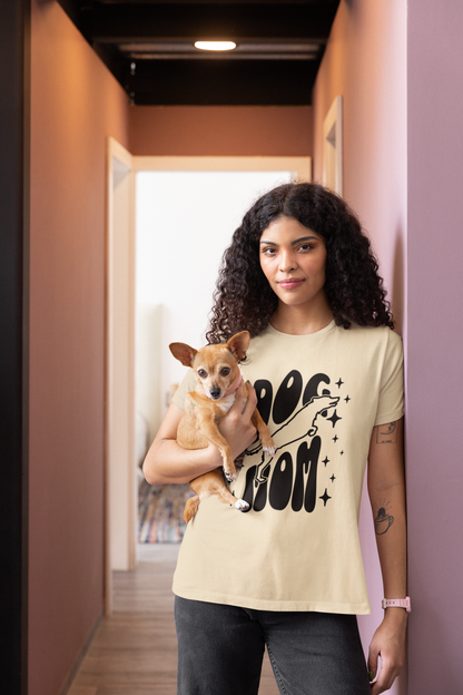 Woman holding a small dog in a hallway wearing a soft cream 'Dog Mom' t-shirt.