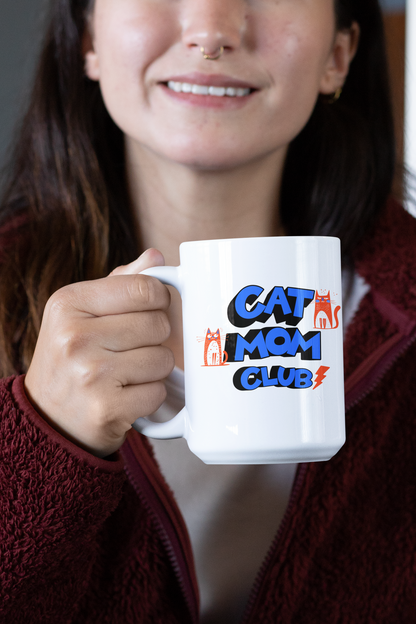 Woman with nose piercing holding Cat Mom Club 15oz ceramic mug — bold retro orange cat design on glossy white ceramic
